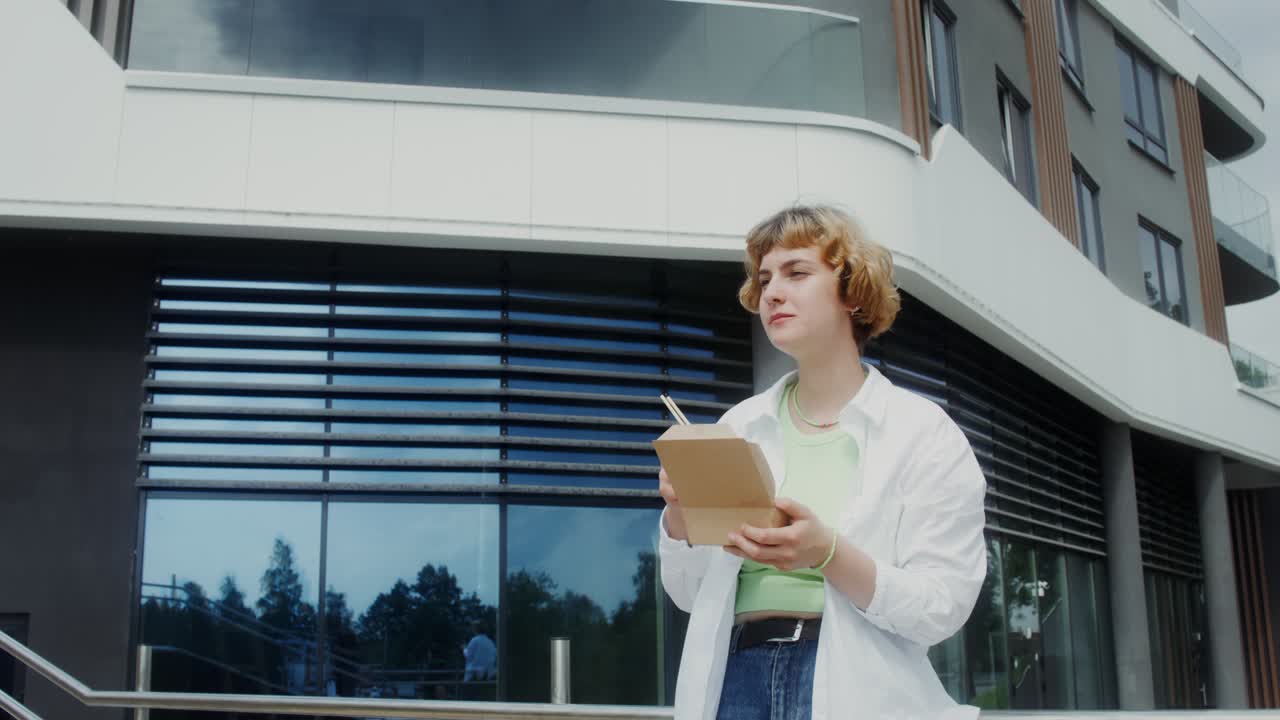 젊은 여성이 현대 건물 밖에서 식사를 하고 있습니다.