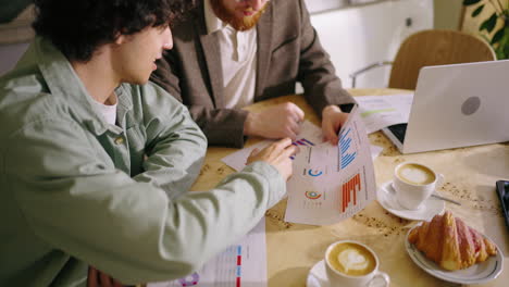 two businessmen analyzing charts during a meeting in a cafe.