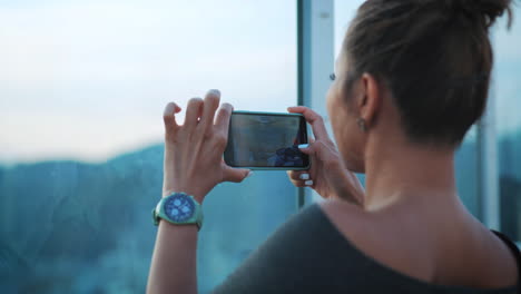 mujer captura paisajes panorámicos de la ciudad usando su teléfono inteligente, se centra en sus manos y teléfono, en un telón de fondo azul de la ciudad suavemente borroso, reflejando su estilo de vida moderno