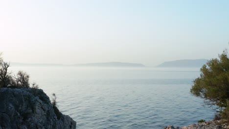 low aerial dolly shot backing up over cres island, croatia with two outcroppings framing another island in the distance