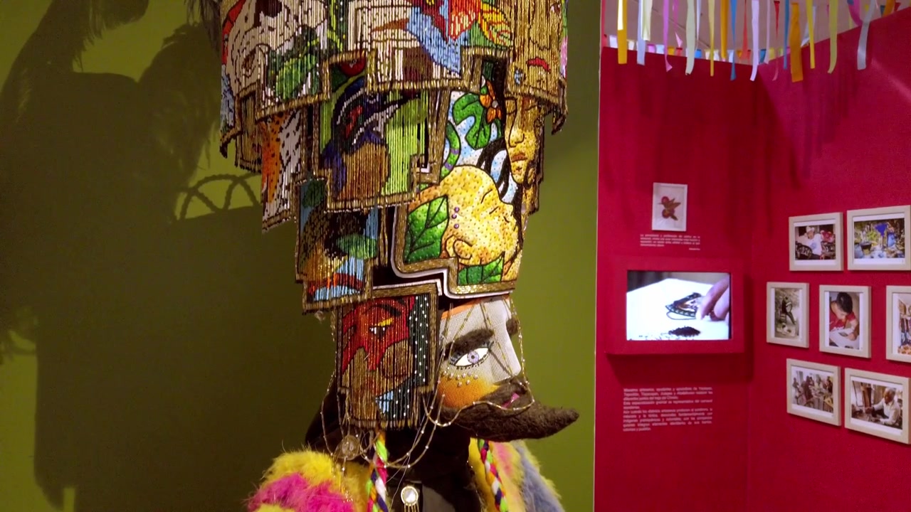 Inquadratura in tilt-up di un costume cerimoniale tradizionale messicano con tessuti colorati, maschera decorativa e copricapo ornato, esposto in una mostra museale in Messico.