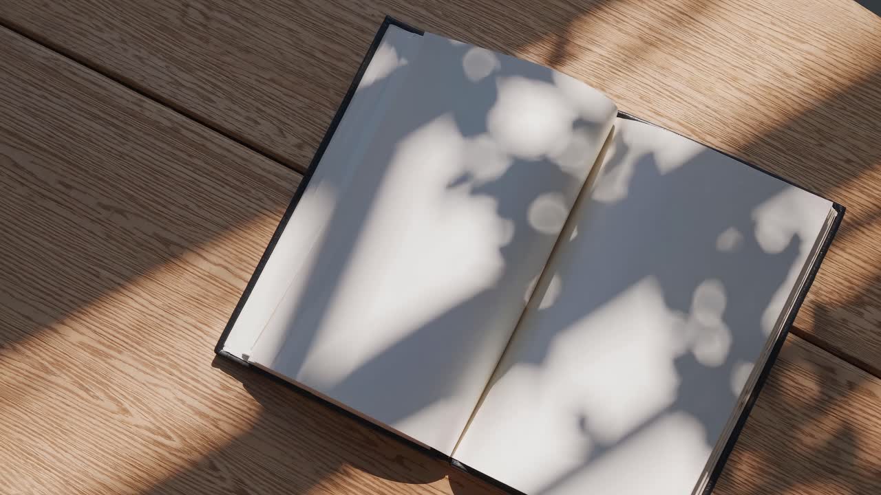 Top-down video of an open book on a wooden table, with soft, dappled sunlight creating abstract