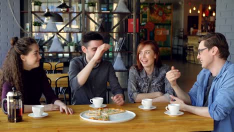 happy handsome guy is telling funny story to his friends while dining in cafe while his mates are laughing and doing high five. friendship and communication concept.