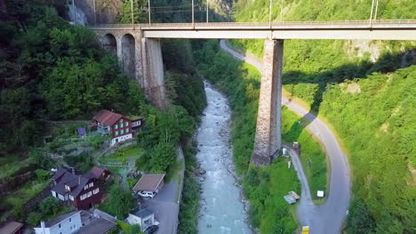 mountain bridge over rocky stream passing by the houses on foothill in lugano, switzerland. - aerial pullback