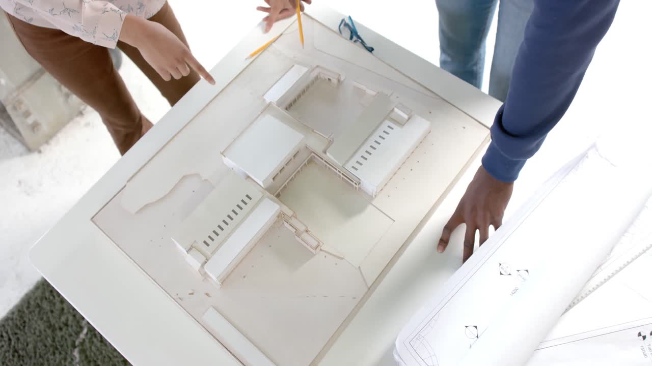 Diverse architect colleagues discussing work at table with building model in office in slow motion