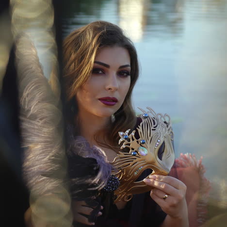 sexy woman closes her face with the carnival mask on the blurred background. beautiful young lady in holiday make up looking at camera. close-up
