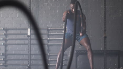 man in gym wearing blue tank top and shorts using battle ropes