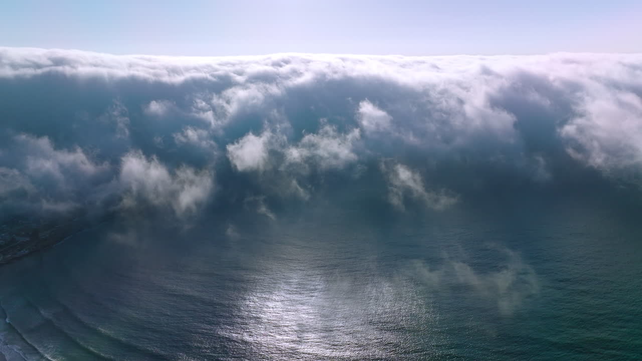 Thick white fog spreading to the coastline from water. Amazing cloudscape of haze on sunny summer day. Aerial view.