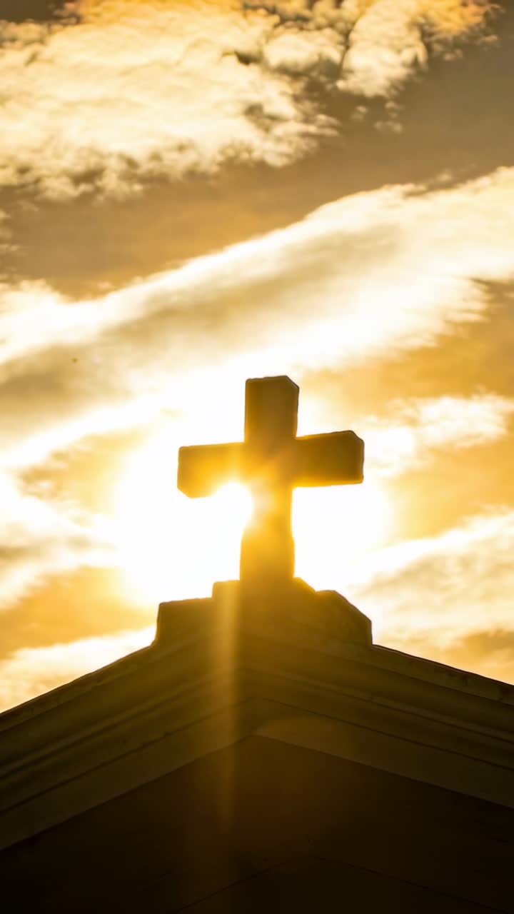 Video verticale: Il sole si posiziona dietro una croce di pietra, creando un'alone sul tetto del campanile e formando un raggio di luce.