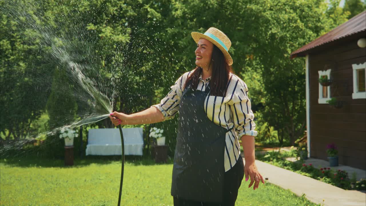 Woman watering garden plants with hose in sunny backyard, showcasing vibrant greenery and joy