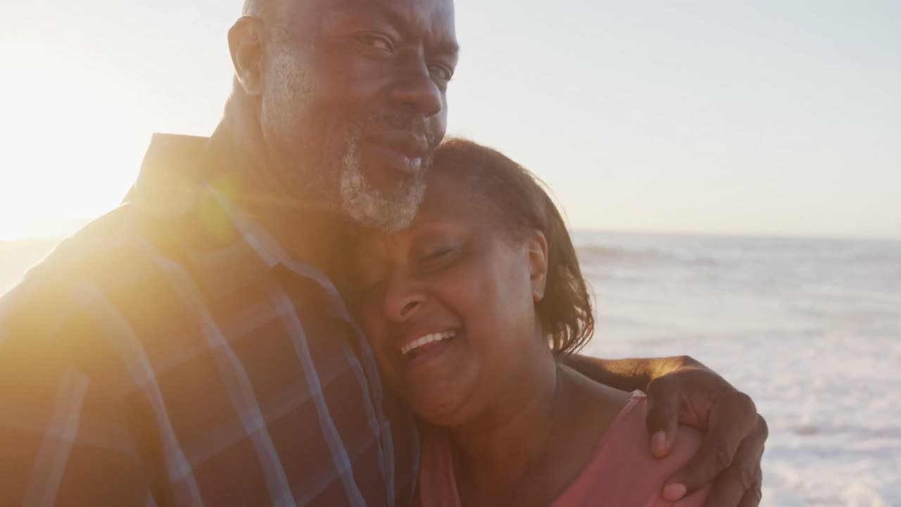 Smiling senior african american couple holding hands and dancing on sunny beach