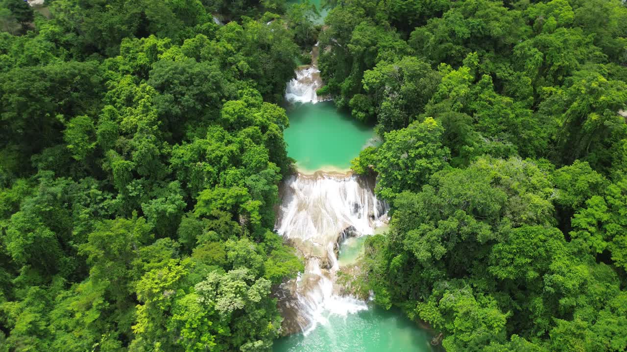 Aerial medium high angle orbit of Roberto Barrios waterfalls flowing through lush forest and turquoise pools