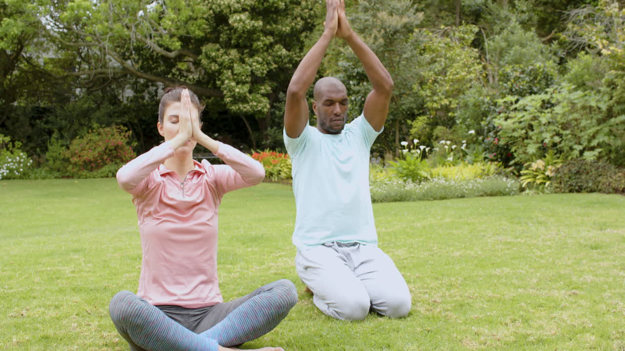Diverse multiracial couple practicing yoga in peaceful garden, focusing on mindfulness together