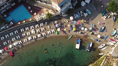 zoom in aerial drone shot a pebble beach with colourful umbrellas, boats, empty sunbeds, swimming pool and a resort, with long shades, a sunset nostalgic summer aesthetic