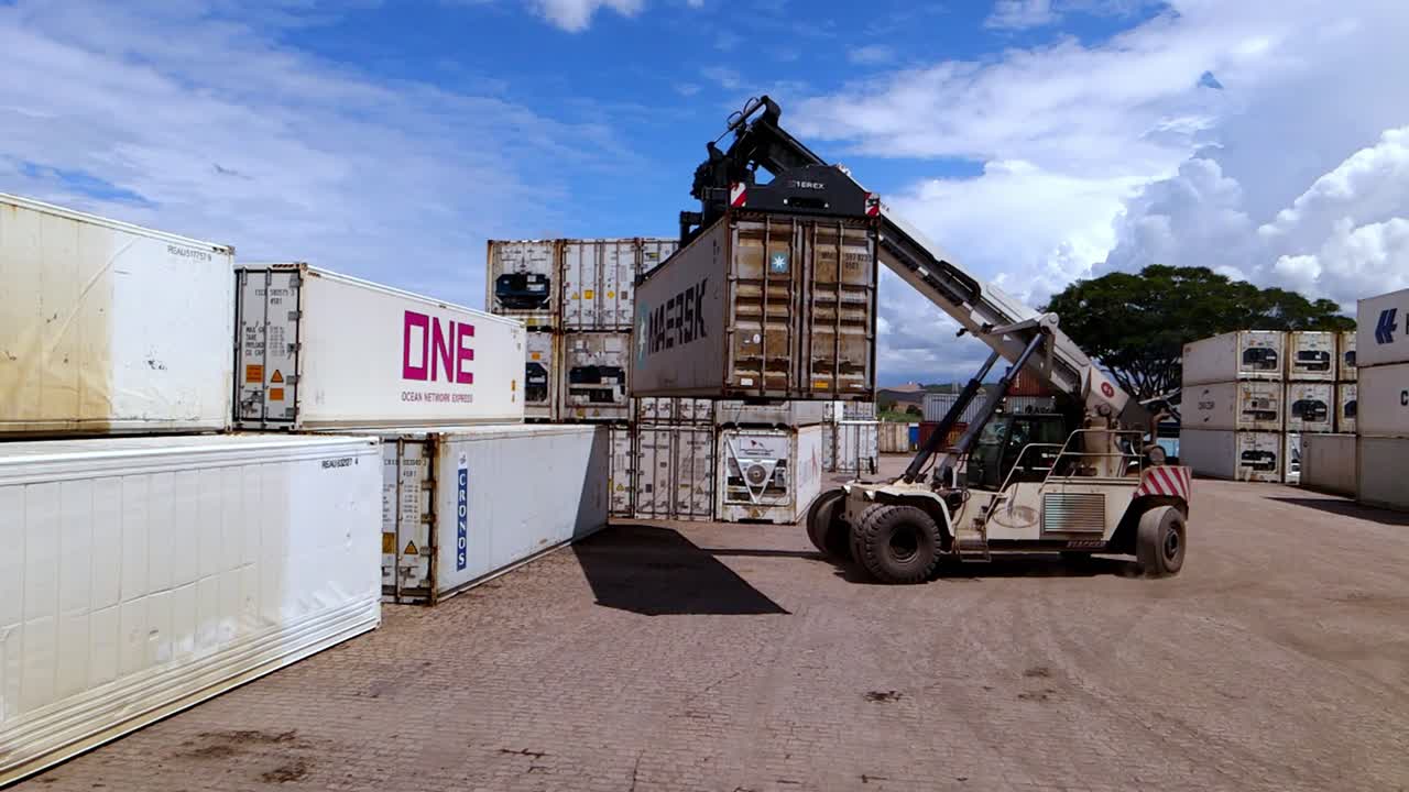 Heavy machinery crane operator removes stacked shipping container, prepare to load