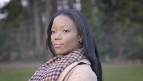 Attractive-black-woman-turning-head-looking-sitting-on-bench-in-park-cloudy-cold-day-central-London