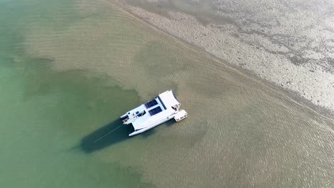 Drone captures a catamaran in shallow waters during golden hour, highlighting serene coastal beauty and tranquil marine environment