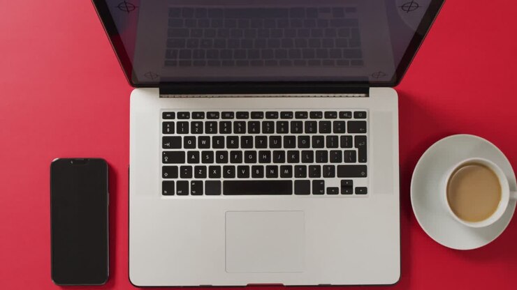 Draufsicht auf Laptop mit Smartphone und Kaffee auf rotem Schreibtisch