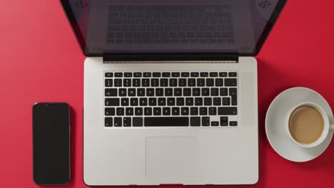 Overhead-view-of-laptop-with-smartphone-and-coffee-on-red-desk