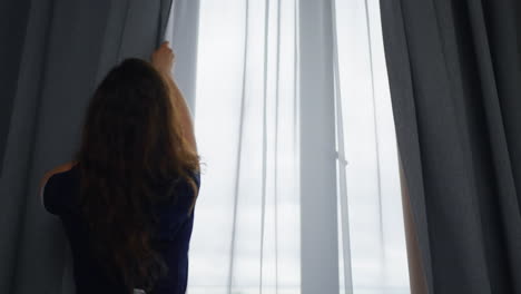 a woman opens the curtains in her bedroom and looks out the window