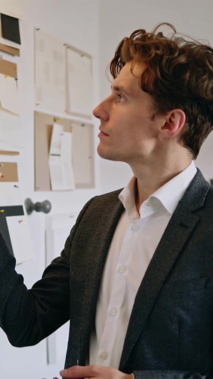 Video verticale: Vedendo un campione, una designer in blazer sistema una tavola nello studio, pianificando, con spazio per il testo