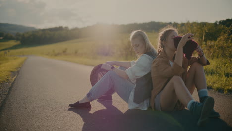 bored women with hats sitting on road near meadow