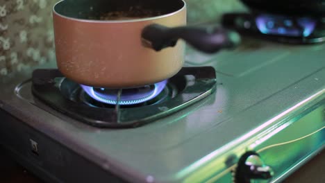 Kitchen-one-small-burner-turning-on-stove,-cooking-home-flame,-hand-turns-natural-gas-with-pan