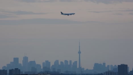 commercial aircraft flying above silhouette of toronto skyline