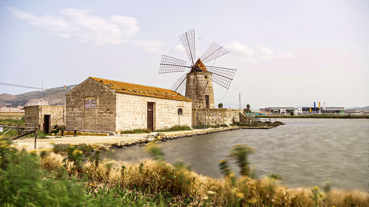 gente viendo el edificio antiguo con molino de viento en la reserva de salinas durante el día soleado en sicilia