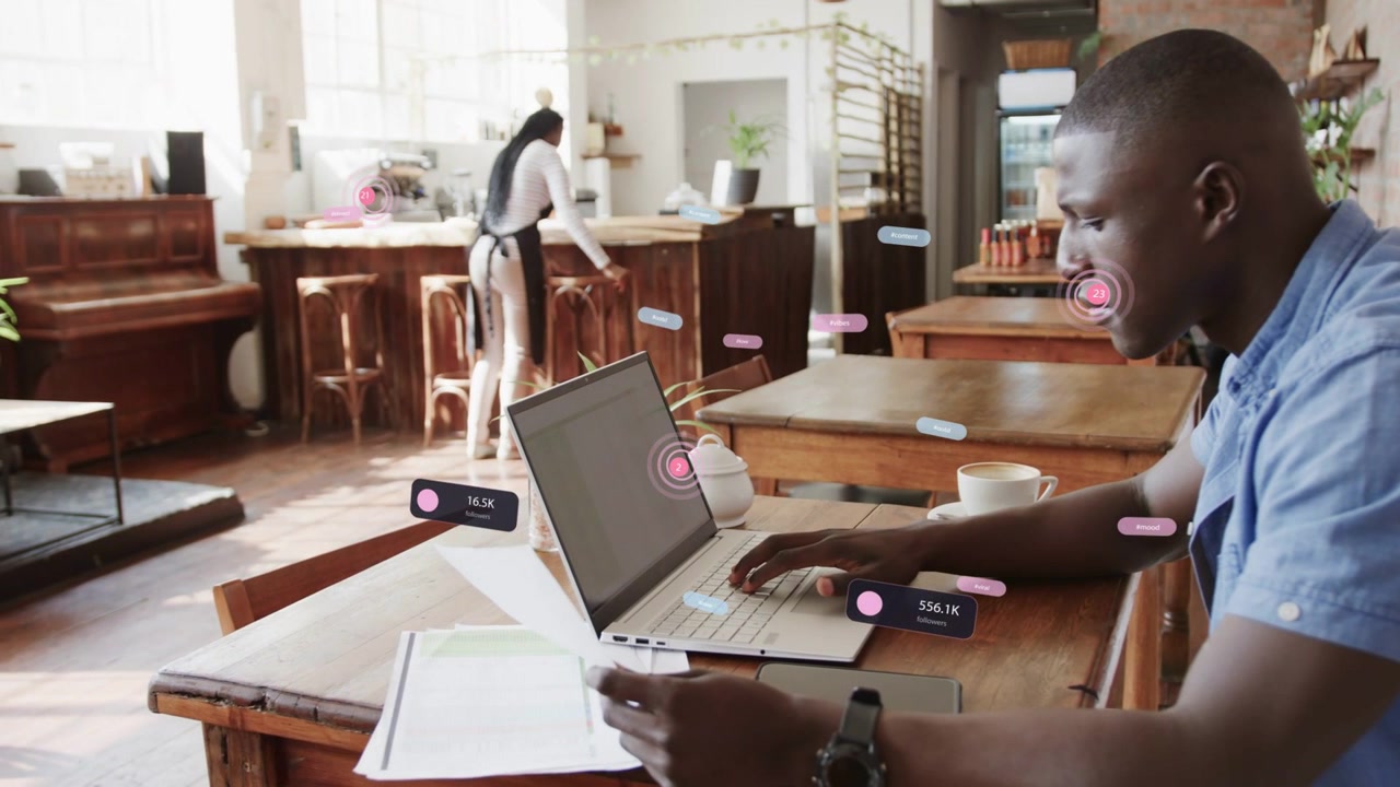 Seated man typing and scanning paper, causing pink UI badges over laptop for business analytics