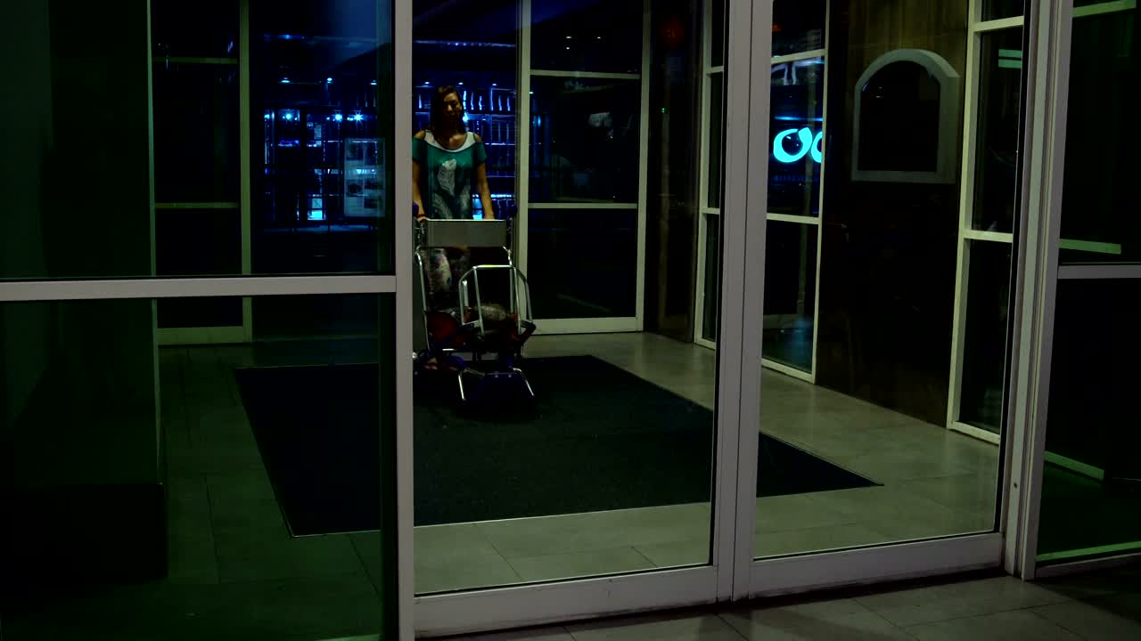 한 여성이 자동 문을 통해 짐을 가진 카트와 함께 건물로 들어갑니다.