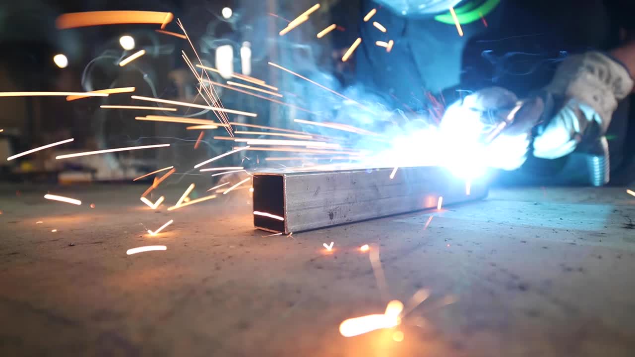 Welder in protective helmet welding metal detail in workshop