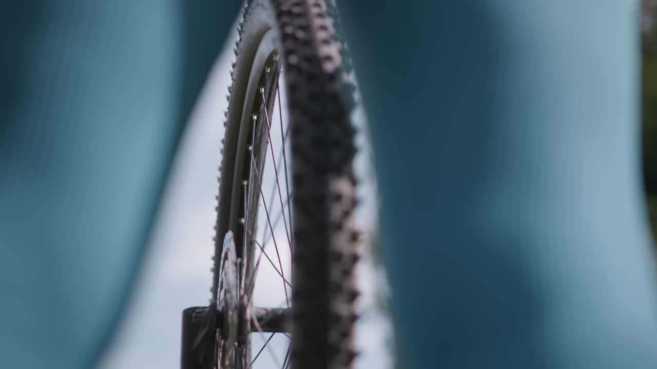 Bicycle wheel passes, Bike wheel quickly moves past woman, Cyclist wheel rapidly overtakes woman strolling along trail, Bicycle wheel rushes past woman walking along trail with quick speed