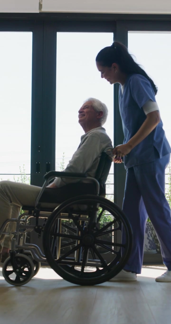 Nurse Pushing Senior Man in Wheelchair Through Bright Room