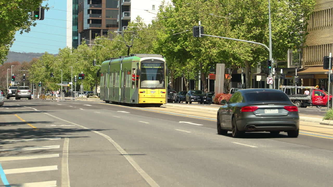 A green and yellow tram driving down the road in a busy city. This modern tram is an efficient way to commute in the city.