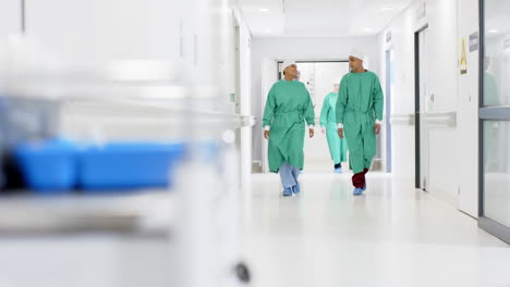 Diverse-male-and-female-surgeons-wearing-surgical-gowns-walking-in-corridor-at-hospital,-slow-motion