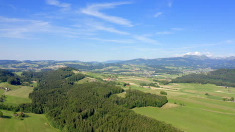 swiss countryside with lush green fields and forest under blue sky in vaud, switzerland - aerial drone shot