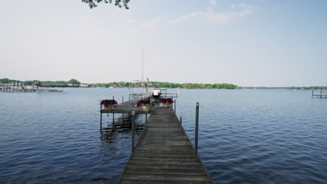 Gimbal-push-in-shot-of-a-boat-dock-on-a-lake-with-flower-pots,-jet-ski-lift,-and-an-empty-boat-lift