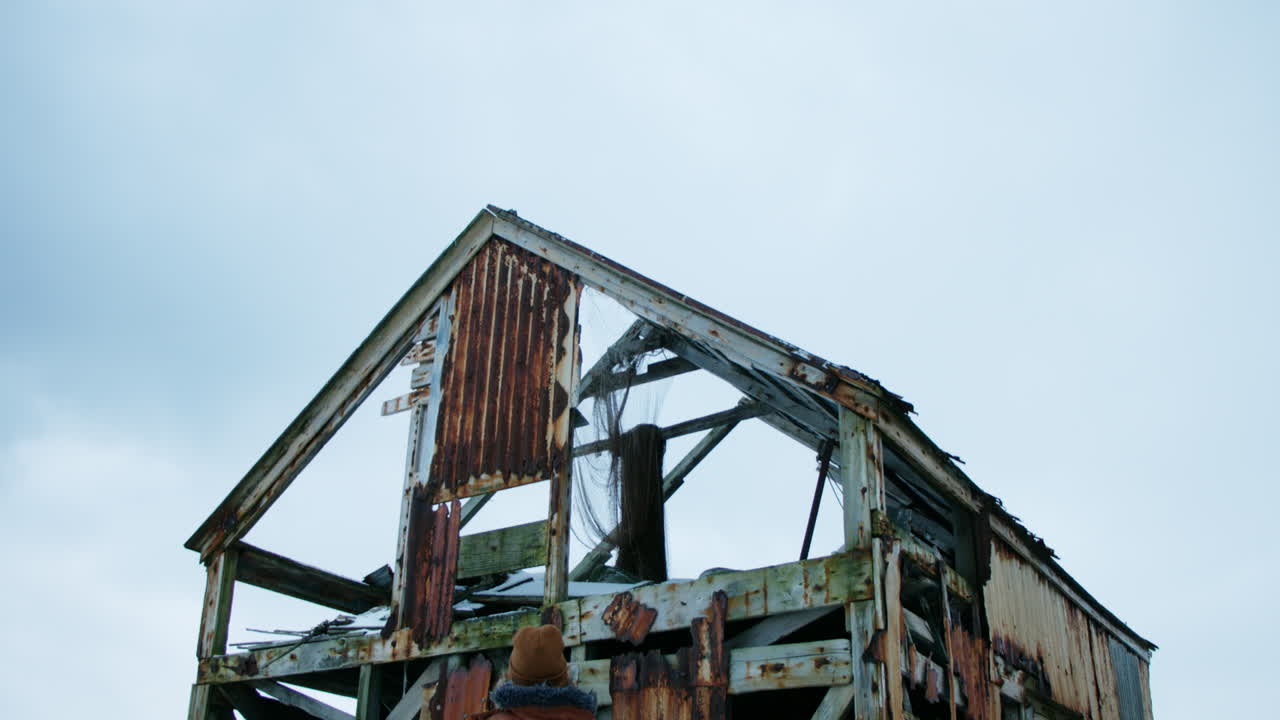 Slow tilt unveiling a girl standing near the ruins of a damaged farm.