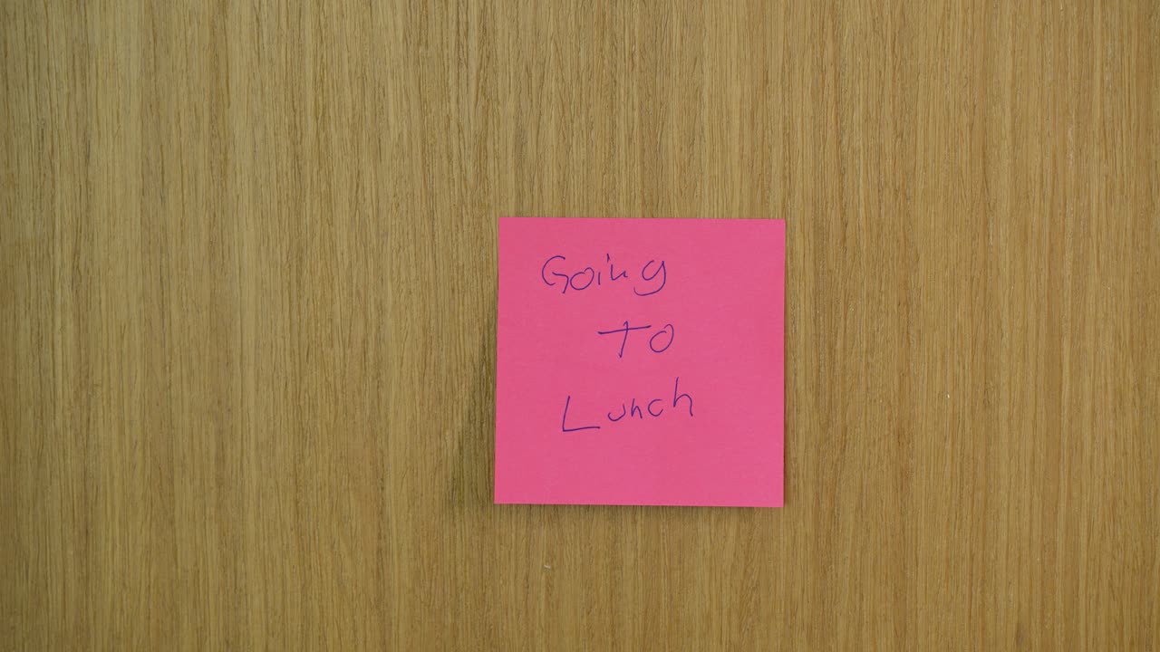 Detailed close-up of a wooden door as a post-it, sticky note saying 'Going to Lunch' is removed. Warm lighting emphasizes texture, offering an intimate view perfect for office or business themes
