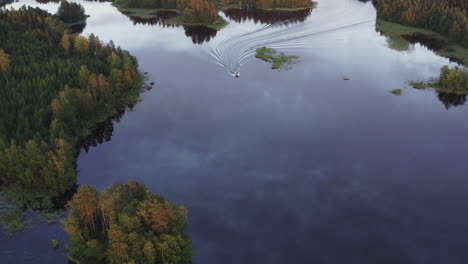 drone video of a motorboat cruising on a calm lake surface by golden hour sunset, between small islands, heading towards camera