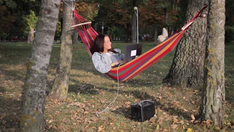woman working on laptop in a hammock in a park