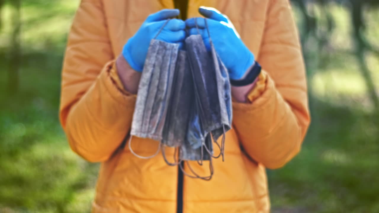 Man in medical gloves holding a bunch of dirty medical masks raised from the ground. Pollution idea