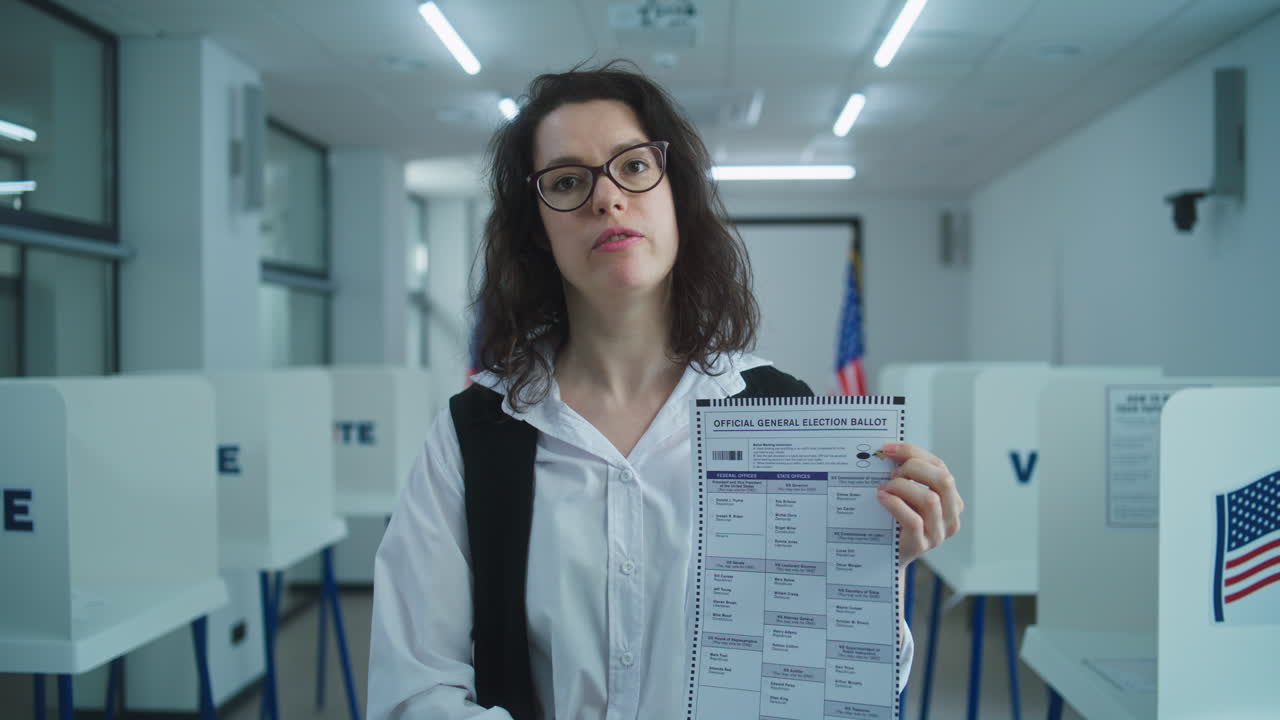 American Woman Speaks on Camera Shows Paper Bulletin Calls for Voting American Woman Speaks on Camera Shows Paper Bulletin Calls for Voting National Elections Day in the United States Voting Booths at Polling Station Concept of Civic Duty and Patriotism Portrait