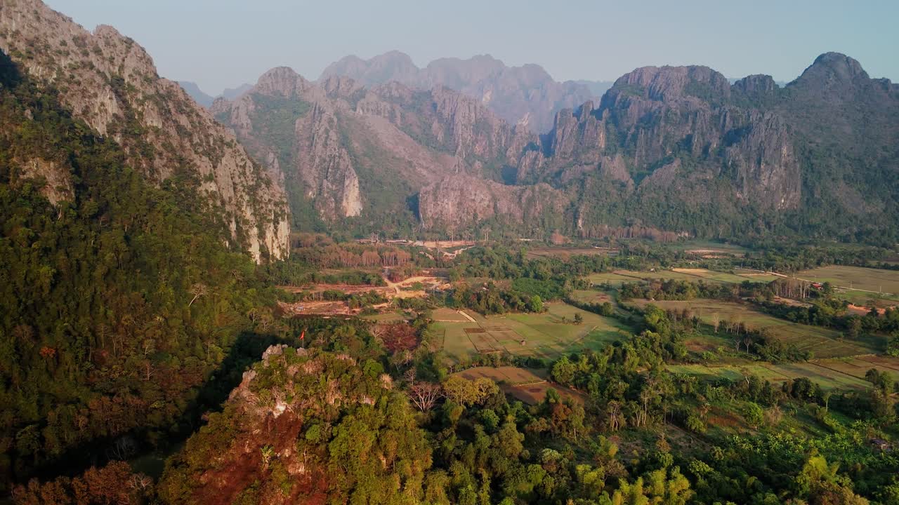 Formazioni calcaree in un paesaggio rurale, con la bandiera del Laos sulla collina