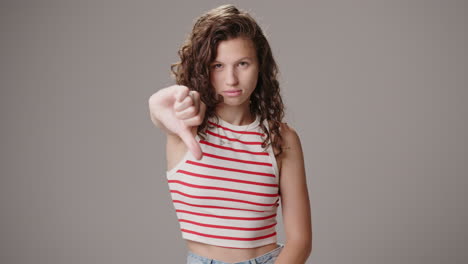 studio shot of young brown-haired woman making thumbs down sign