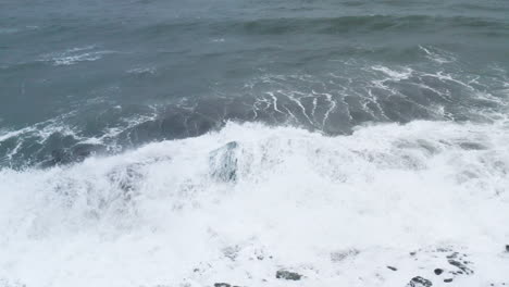 Atemberaubende-Drohnenaufnahme-Von-Wellen,-Die-Auf-Einem-Wunderschönen-Eisfelsen-Am-Diamond-Beach-In-Island-Brechen