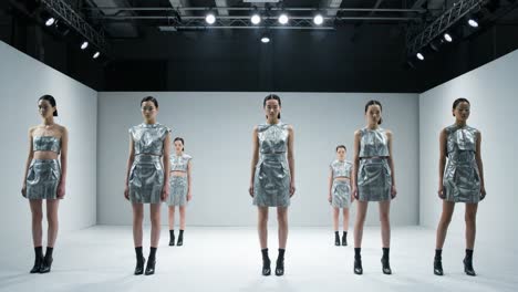 A Futuristic Fashion Presentation Featuring Multiple Models in Metallic Attire Showcasing Modern Style on a Minimalist Runway Stage