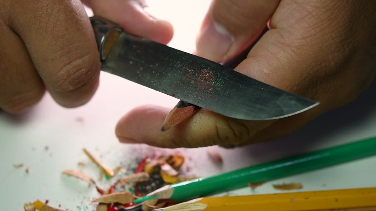 Opptak av hender som sakte spisser en blyant og noen fargeblyanter med en skarp kniv
