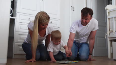 A-family-of-three-in-white-T-shirts-and-blue-jeans-sitting-on-the-floor-of-their-bedroom-playing-with-the-boy-in-intellectual-games.-Slow-motion-shooting-happy-family